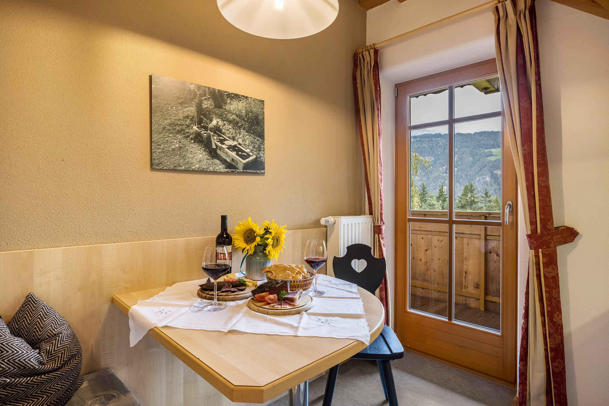 Esstisch mit Wein und Südtiroler Spezialitäten mit Blick auf den Balkon im Apartment Bruneck - Oberplunerhof