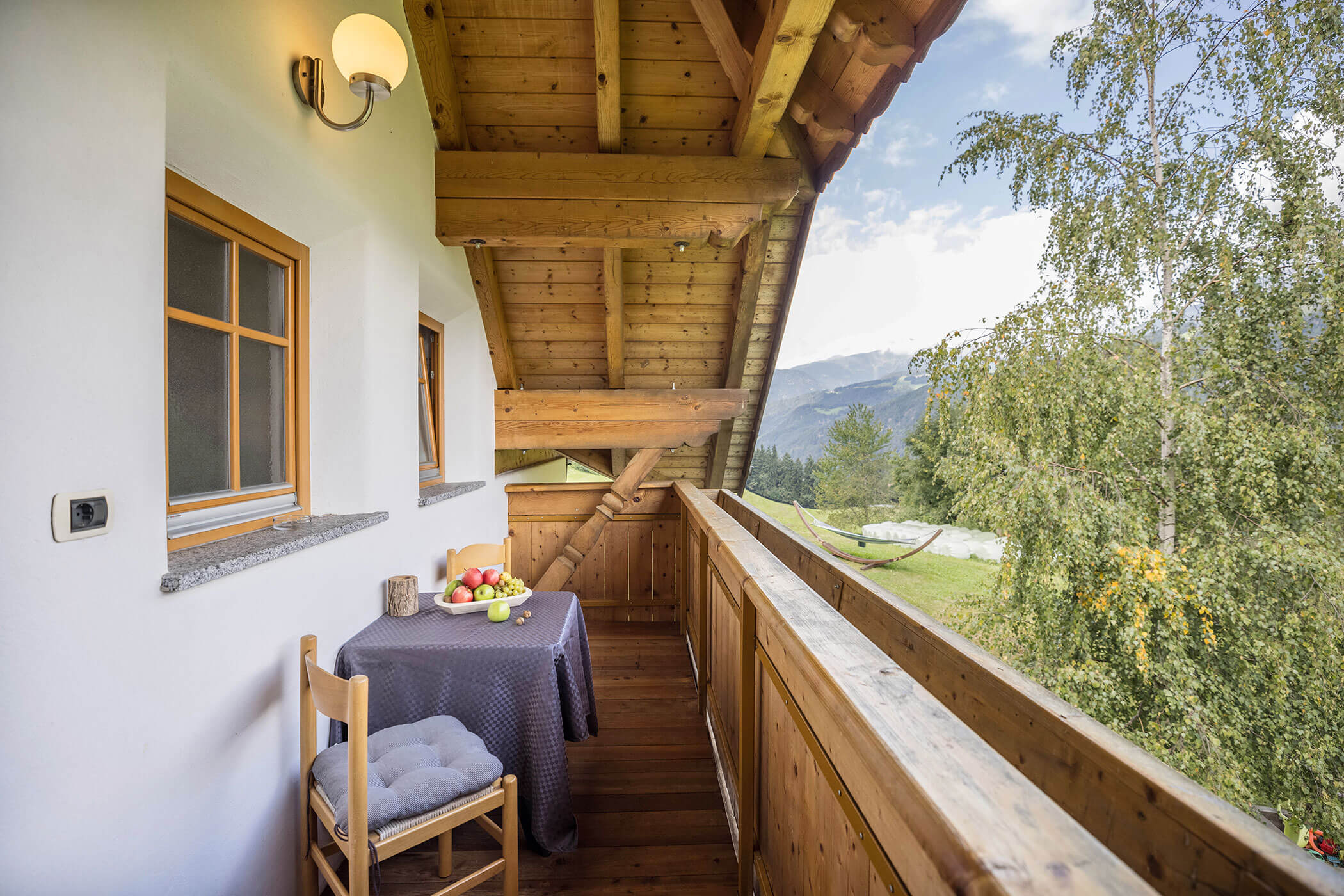 Der Balkon vom Apartment Bruneck mit zwei Stühlen und einem Tisch mit Blick auf die Berge und Bäume - Oberplunerhof