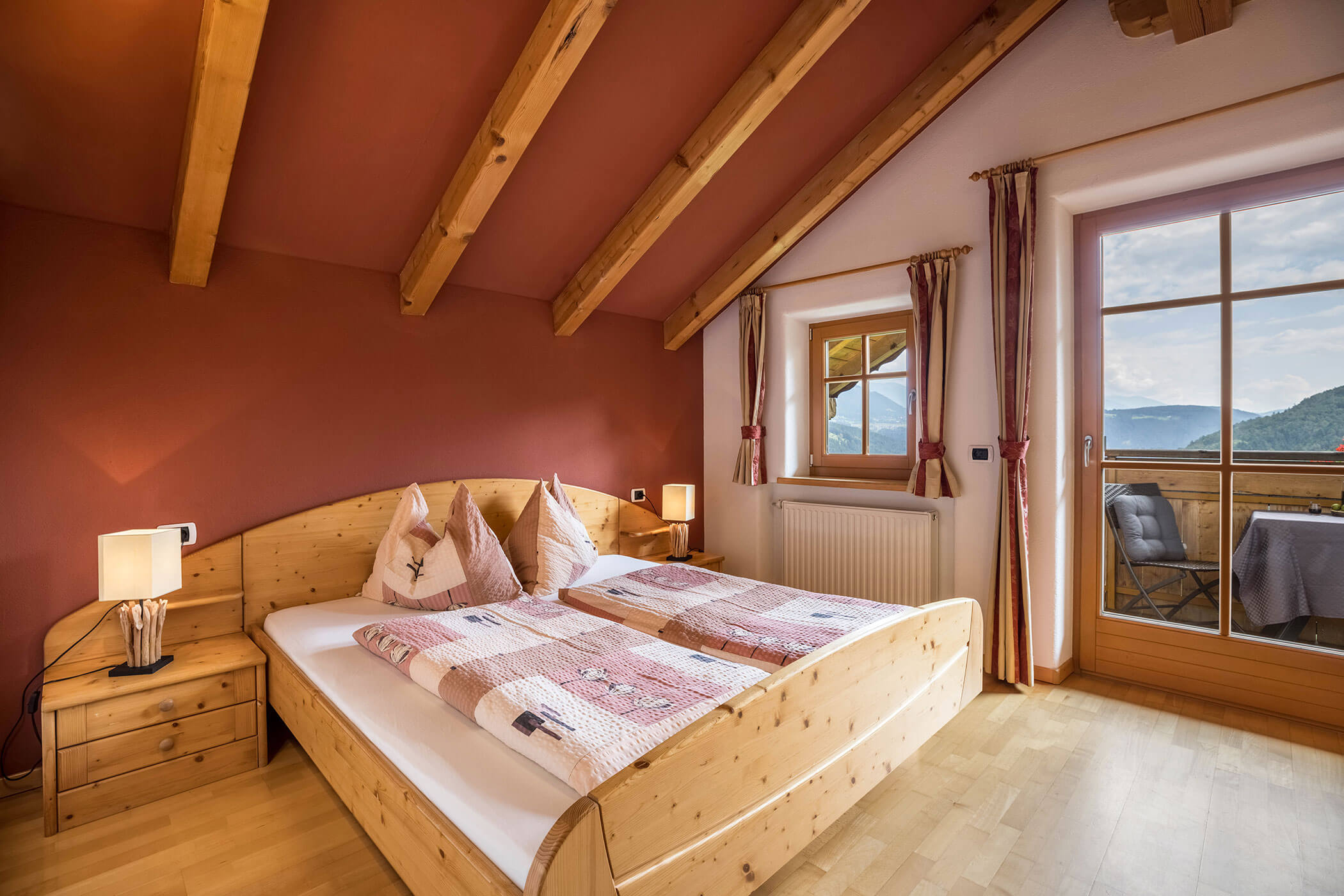 Schlafzimmer im Apartment Bruneck mit Doppelbett und Blick auf den Balkon mit Tisch und Stühlen - Oberplunerhof