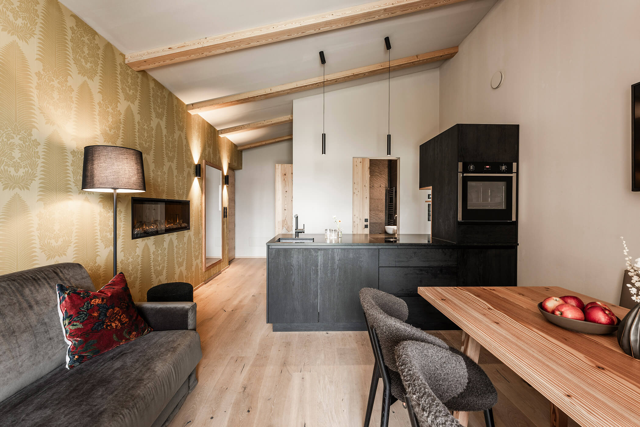 Wohnküche mit dunkler Kochnische, Esstisch und grauem Sofa - Oberplunerhof