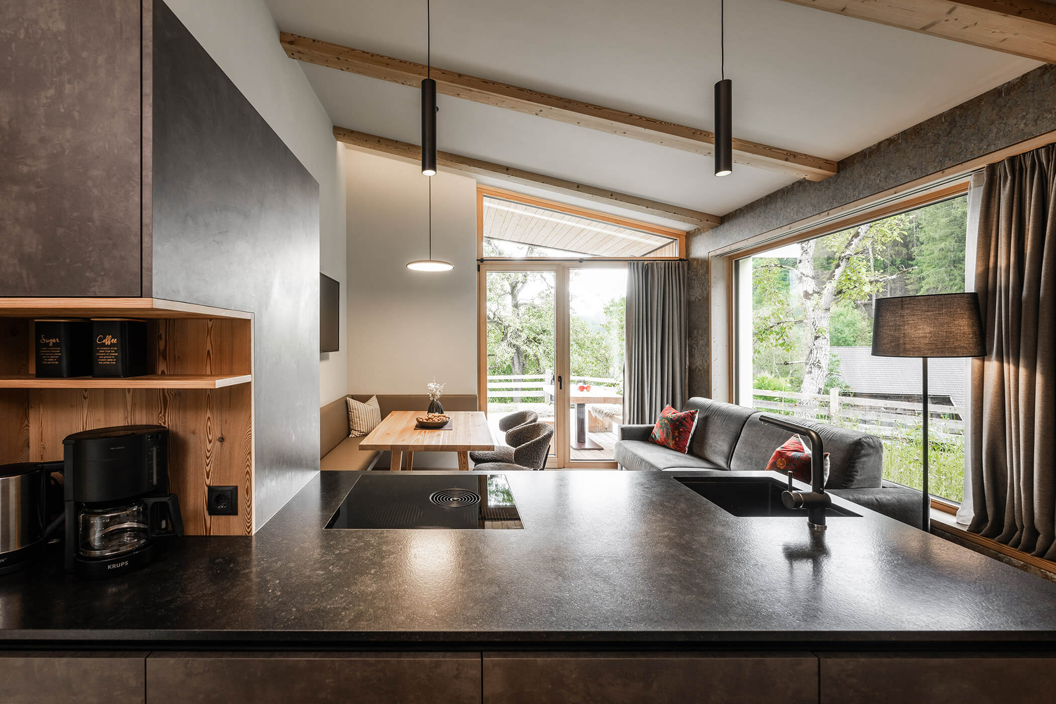 Wohnküche im Chalet Woods mit dunkler Kochnische, Holztisch und Sofa - Oberplunerhof