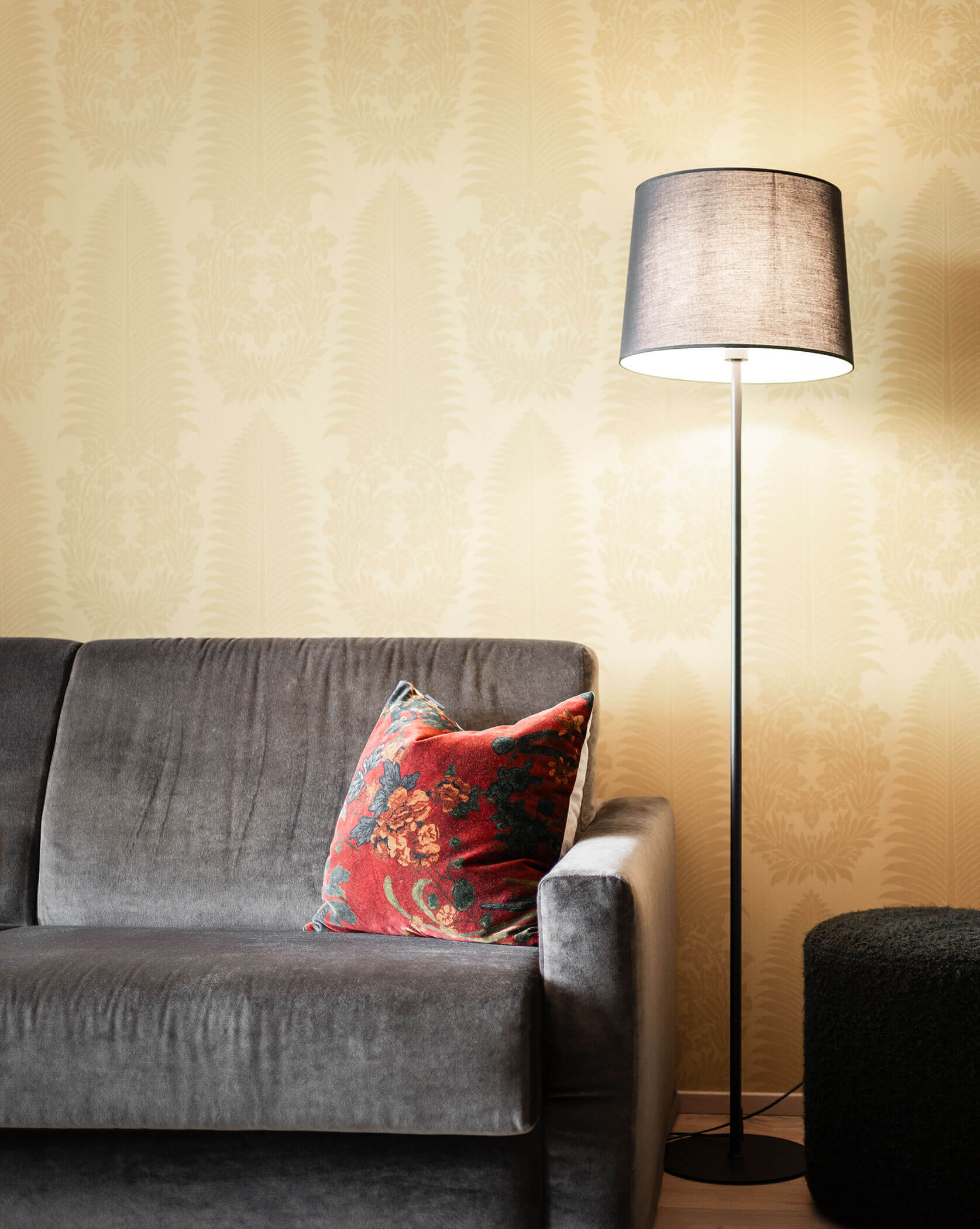 Dunkelgraues Sofa mit einem roten Kissen und einer Stehlampe daneben - Oberplunerhof