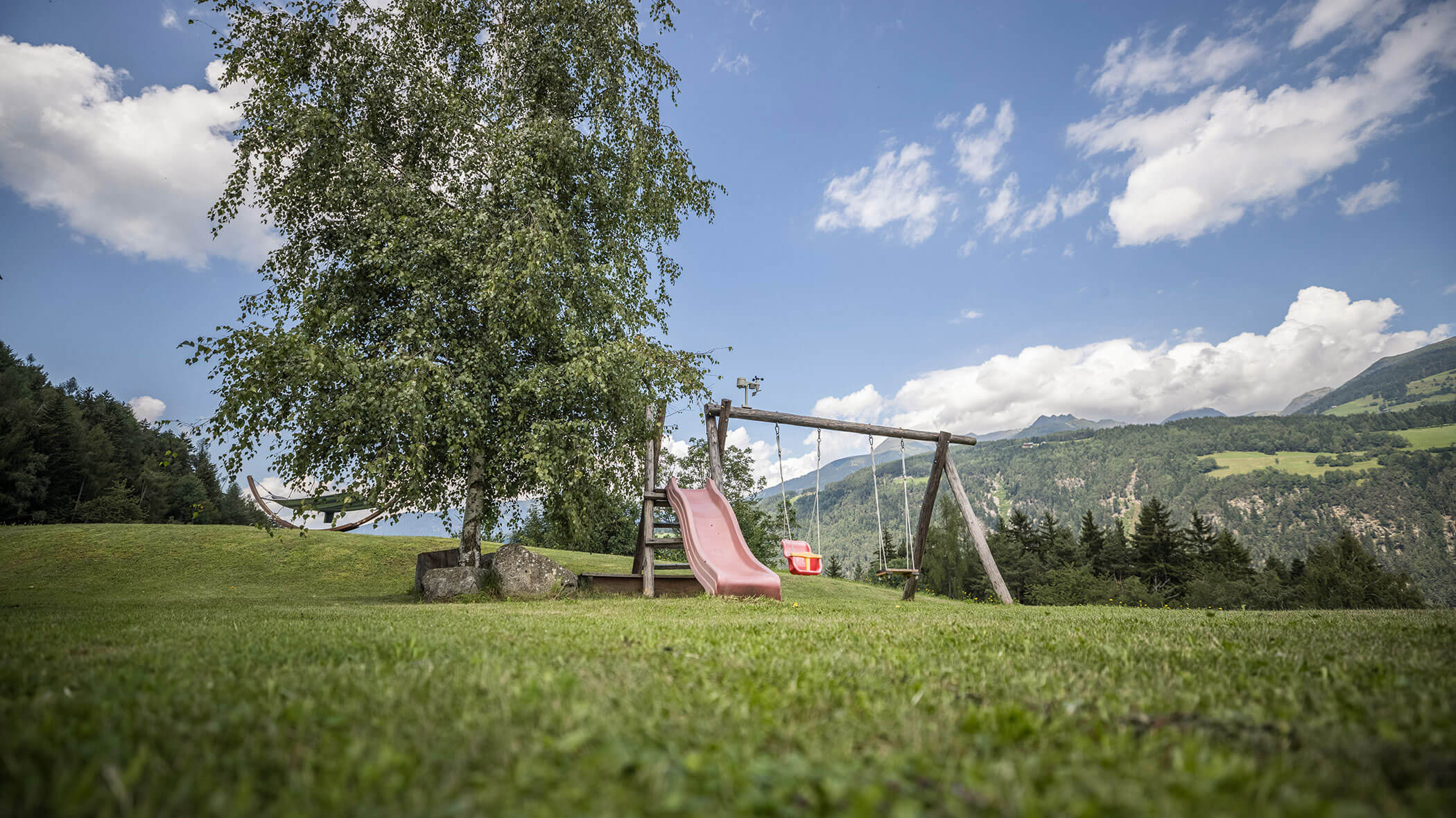 Kleiner Spielplatz mit zwei Schaukeln und einer Rutsche auf einer Wiese mit herrlichem Ausblick - Oberplunerhof