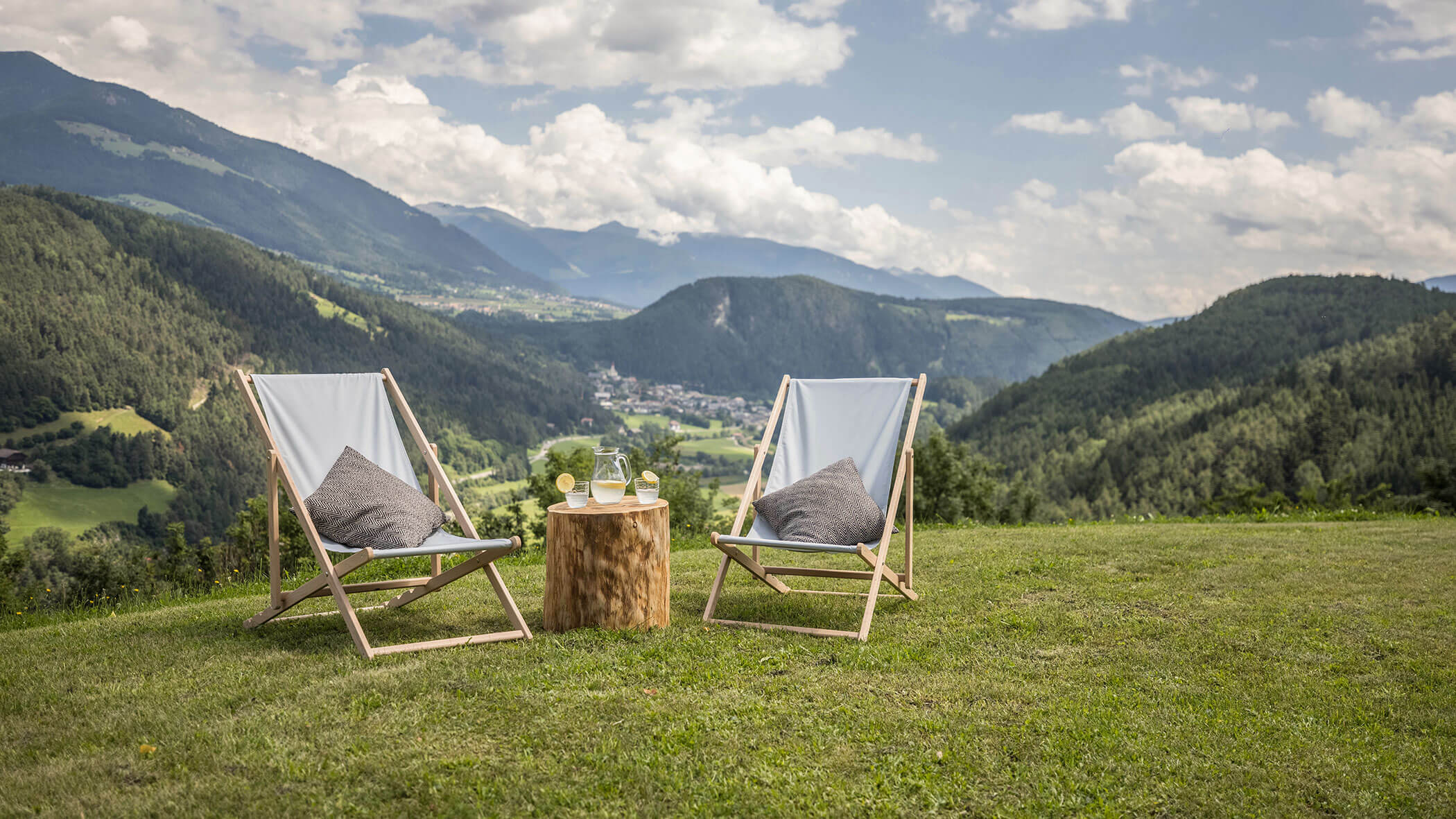 Zwei Liegestühle auf einer Wiese mit frischem Zitronensaft auf einem Baumstamm - Oberplunerhof