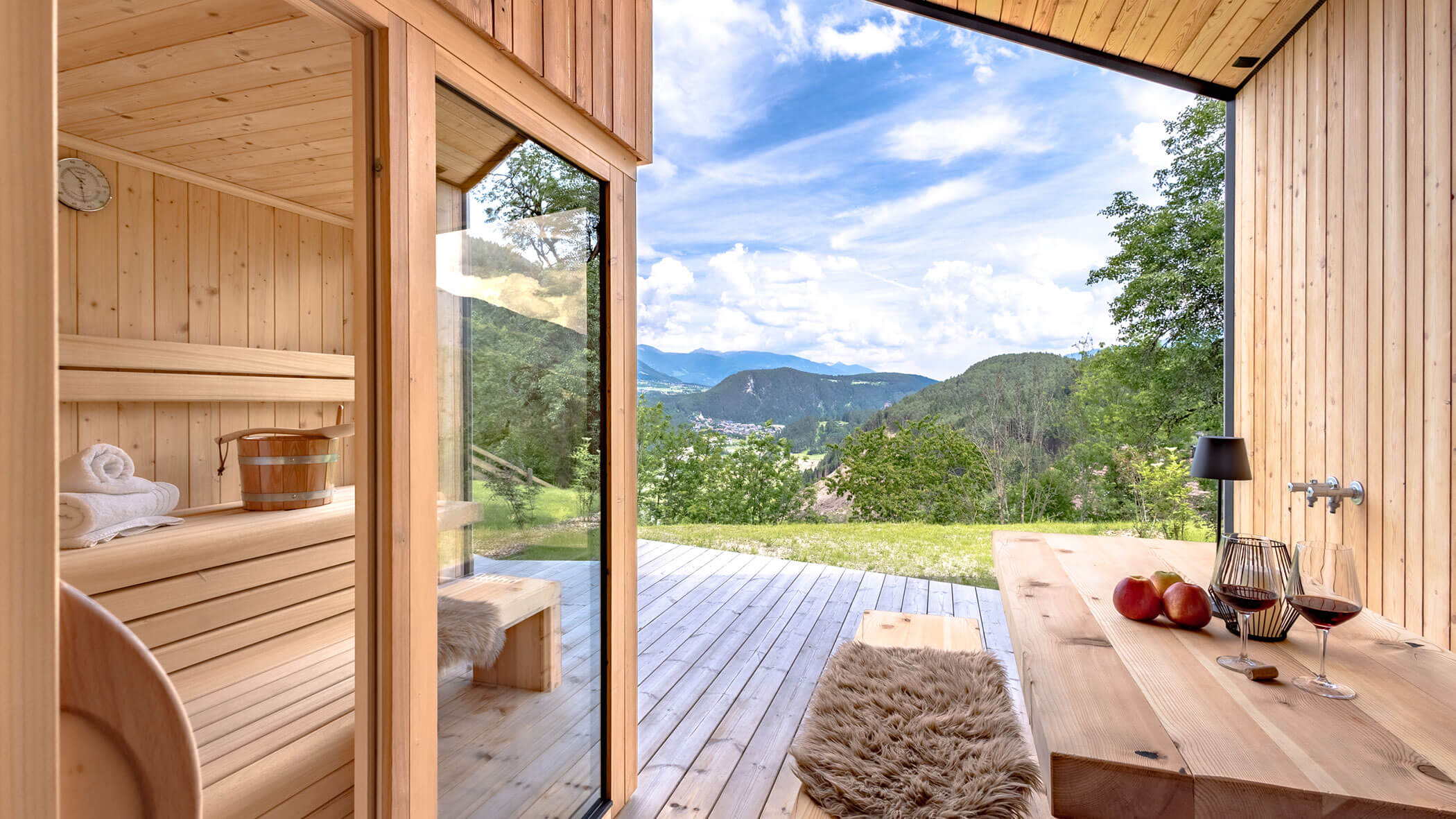 Sauna im Chalet Woods mit Blick auf die Berge, daneben ein Tisch mit zwei Gläsern Wein - Oberplunerhof