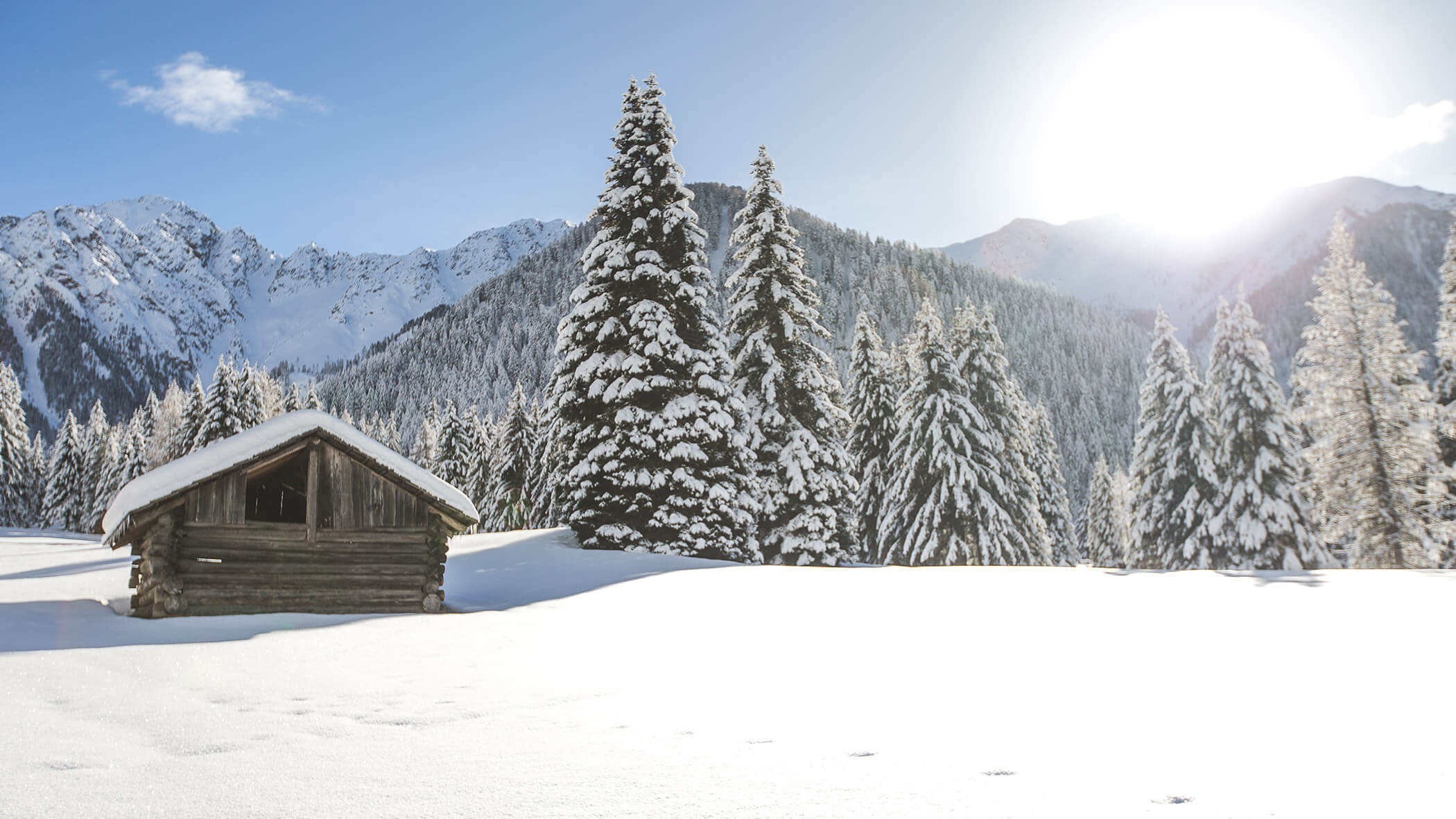 Alte Hütte inmitten einer verschneiten Landschaft mit Bergen und Bäumen - Oberplunerhof