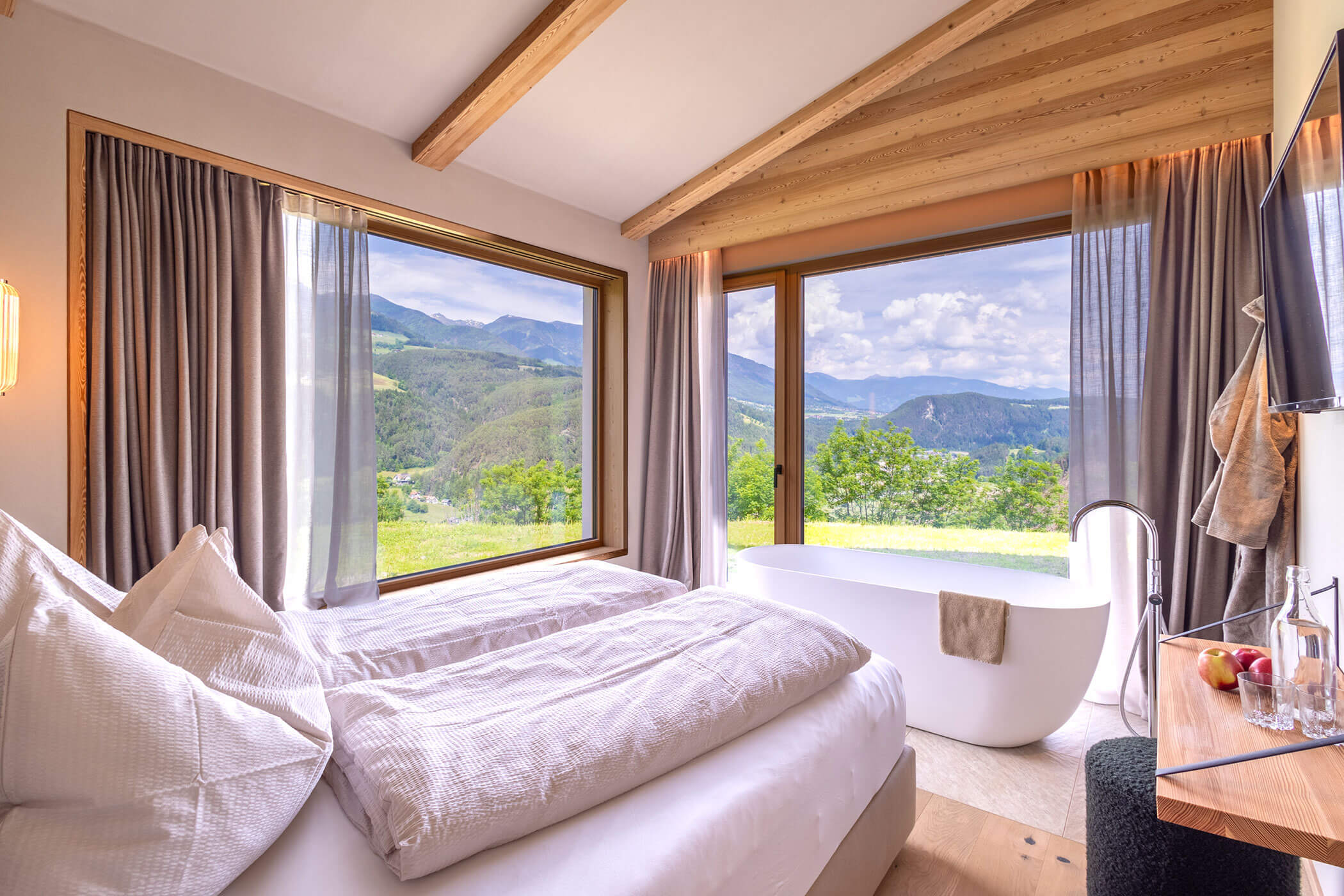 Doppelbett im Chalet Skyline mit freistehender Badewanne, TV an der Wand und herrlichem Blick auf die Südtiroler Bergwelt - Oberplunerhof