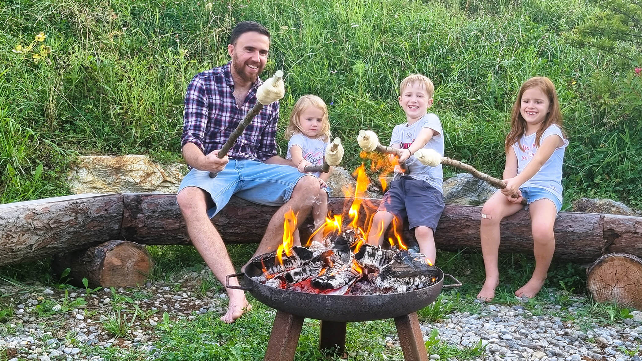 Vater mit seinen drei Kindern vor einer Feuerstelle beim Stockbrot machen - Oberplunerhof