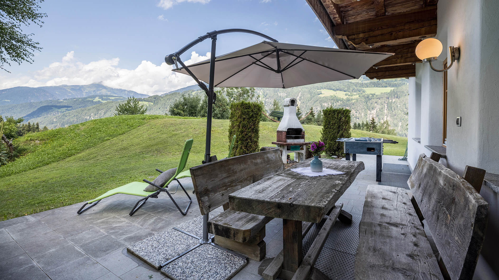 Die Terrasse vom Oberplunerhof mit Holztisch- und Bänken, im Hintergrund ein Grill und Liegestuhl