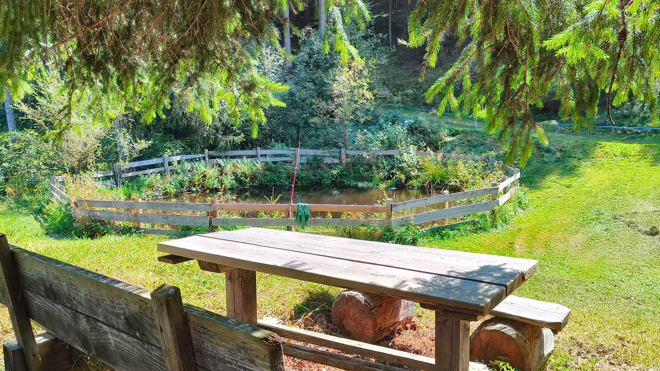 Holztisch- und Bänke vor einem eingezäunten See - Oberplunerhof