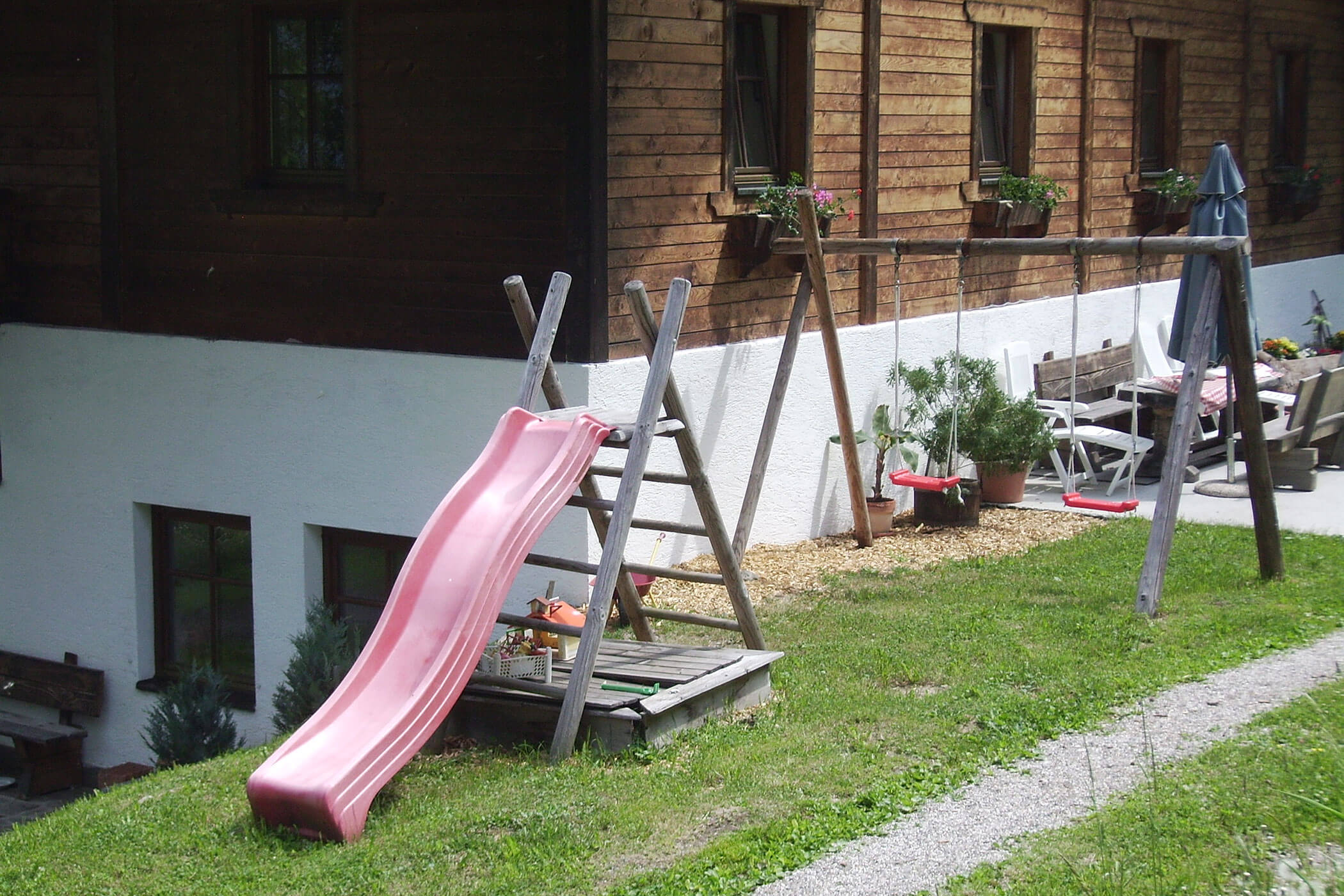 Kleiner Spielplatz mit zwei Schaukeln, Rutsche und einem kleinen Sandkasten vor dem Oberplunerhof