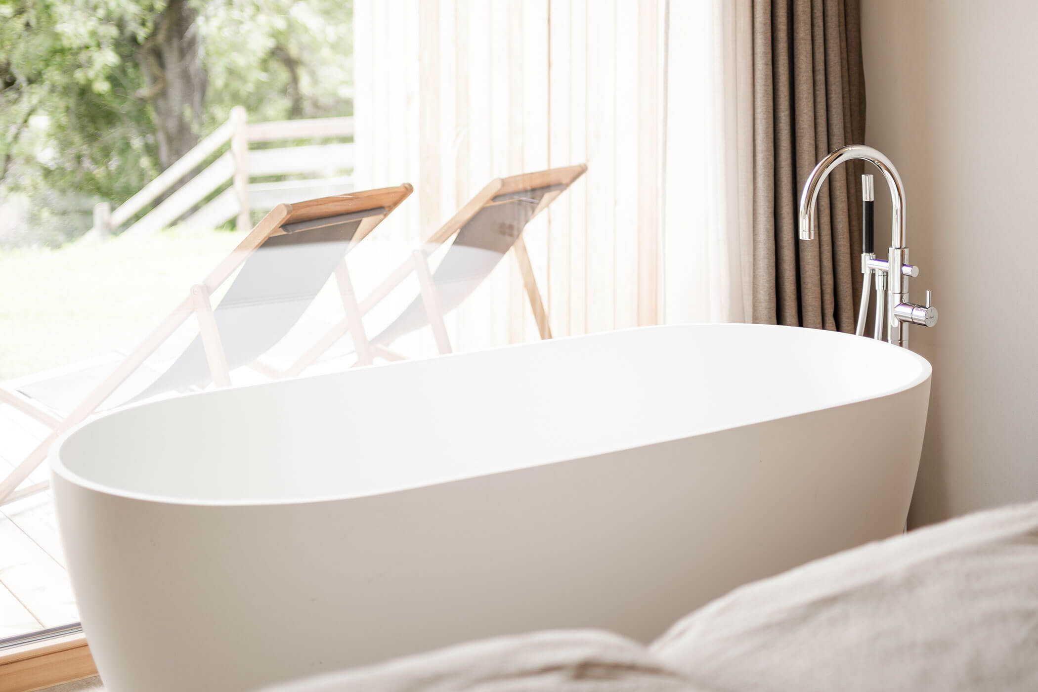 Freistehende Badewanne im Chalet Woods mit Blick auf die Terrasse mit zwei Liegestühlen - Oberplunerhof