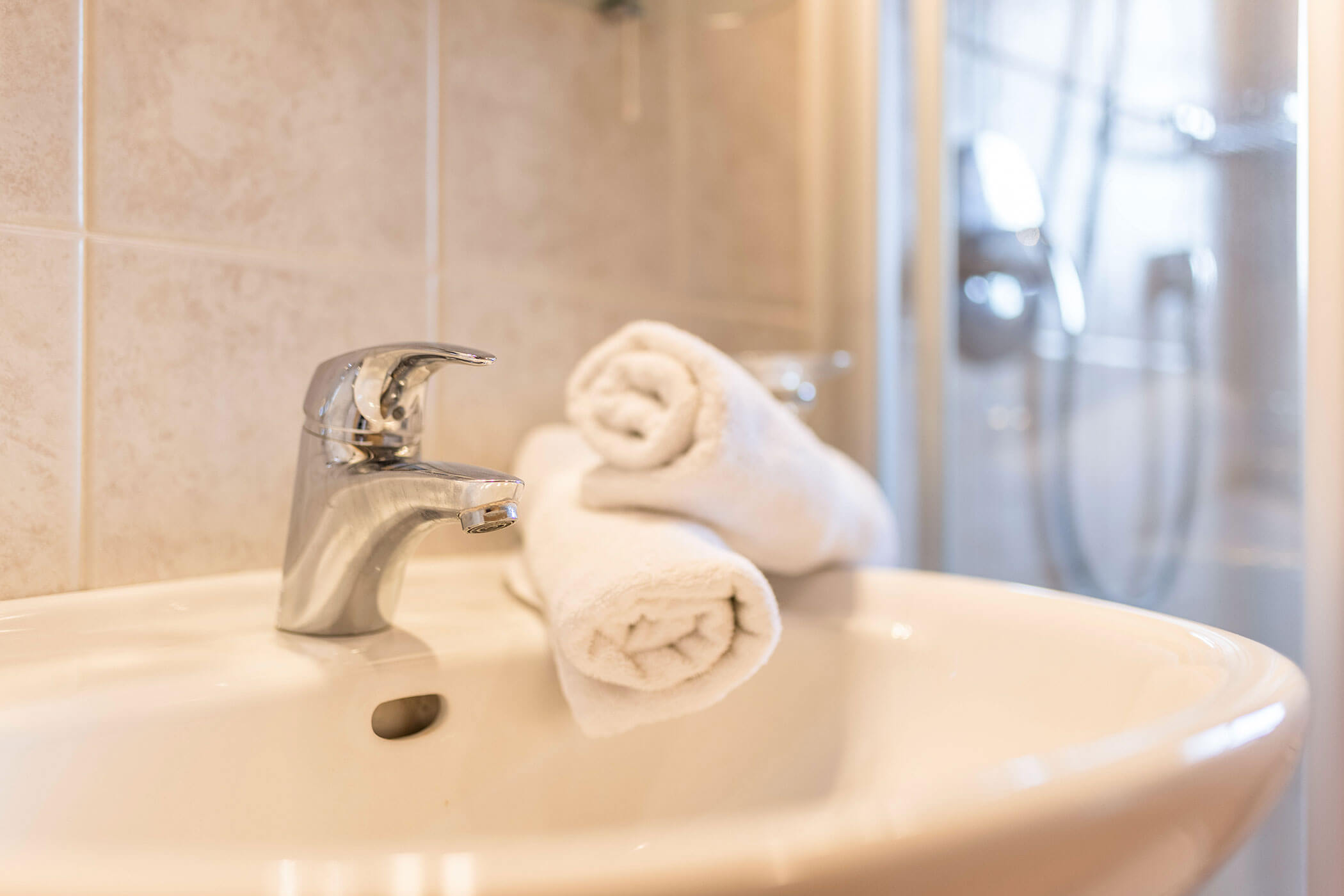 Waschbecken mit zwei weißen Handtüchern, im Hintergrund eine Dusche - Oberplunerhof