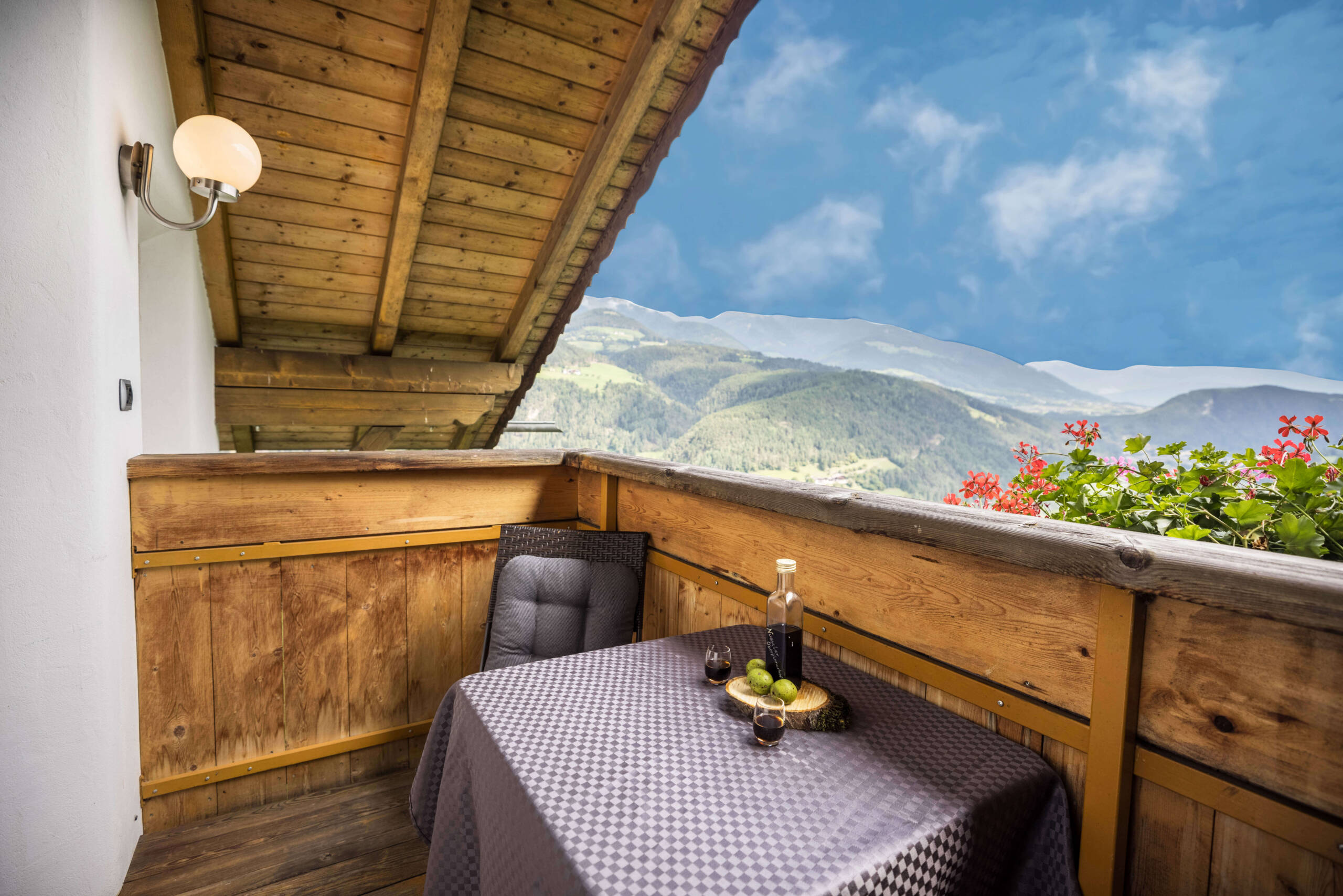 Balkon vom Apartment Bruenck mit einem Stuhl und einem Tisch, darauf eine Flasche Wein, im Hintergrund schneebedeckte Berge - Oberplunerhof