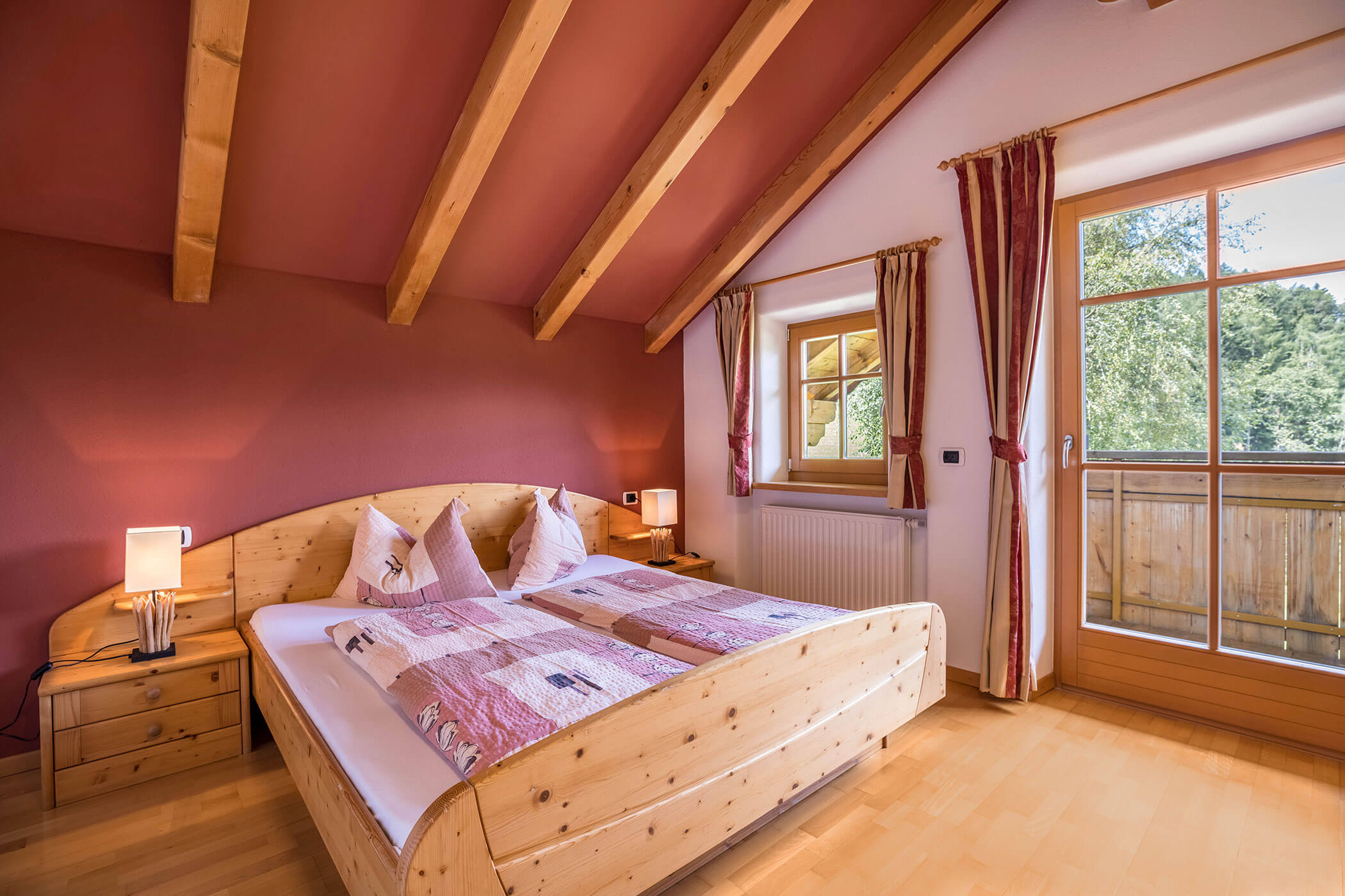Doppelbett im Apartment Bruenck mit Nachttischlampe und Blick auf den Balkon - Oberplunerhof